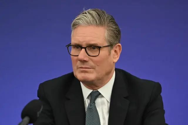 Praịm Minista mba UK Keir Starmer yi uwe ojii nakwa uwe elu na-acha ọcha n'ime ya n'eriri olu efe n'acha ntụ ntụ. Okpu enyo anya. O nwere igwe okwu ojii n'ihu ya