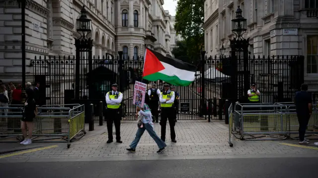 صورة لمتظاهر يحمل العلم الفلسطيني ويعبر شارع الداوننغ ستريت في لندن.