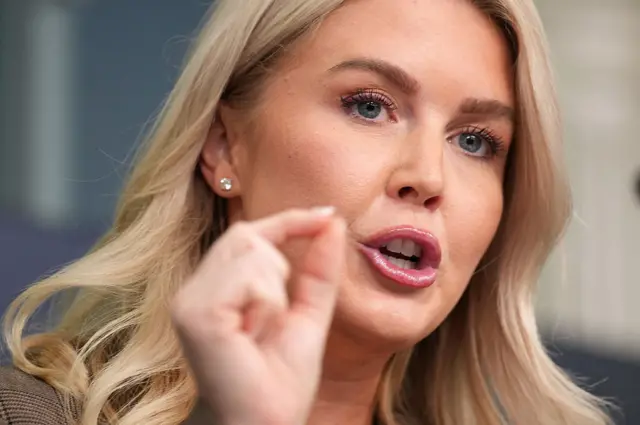 ليفينت شقراء الشعر، عيناها لونهما أزرق. تركز الصورة على وجهها ويدها التي تتحرك أثناء حديثها.