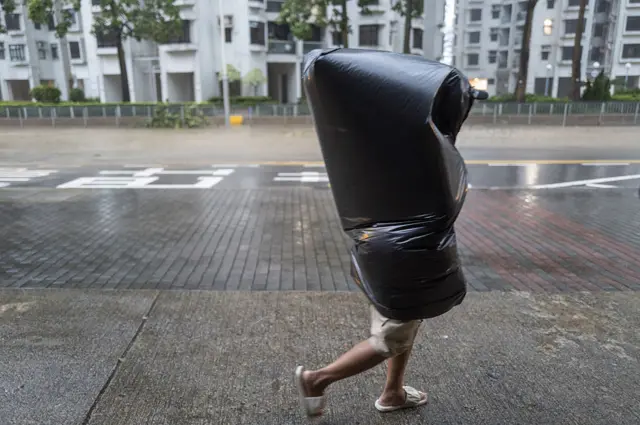 2025年9月24日星期三，一名行人身披垃圾袋在香港杏花邨住宅區避雨。