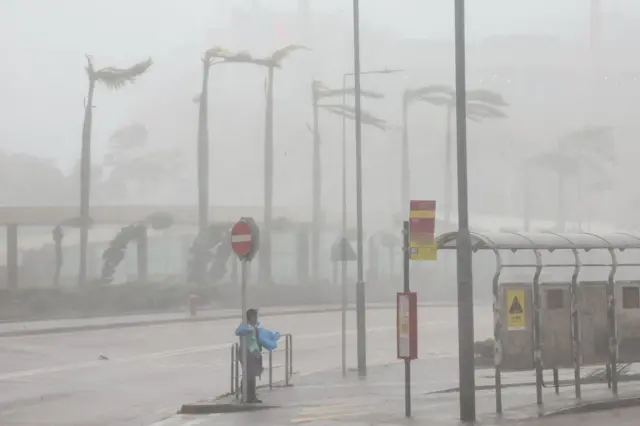 A woman clings to a traffic sign to maintain balance against strong winds from Super Typhoon Ragasa in Hong Kong, China, September 24, 2025.