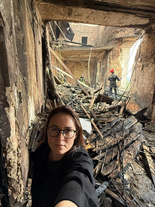 Юлия Свириденко на фоне очень поврежденного помещения, в котором провалена крыша, видны обгоревшие балки