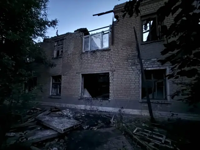 Двухэтажный дом с выбитыми окнами и поврежденной крышей.