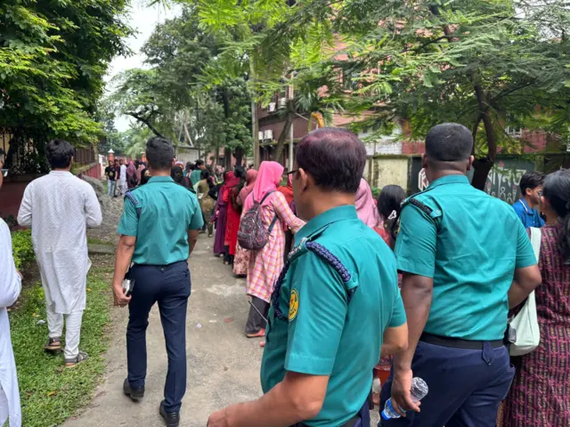 ডাকসু নির্বাচনে ভোট দেওয়ার অপেক্ষায় থাকা ভোটারদের সারির পাশে কয়েকজন পুলিশ হেঁটে যাচ্ছে