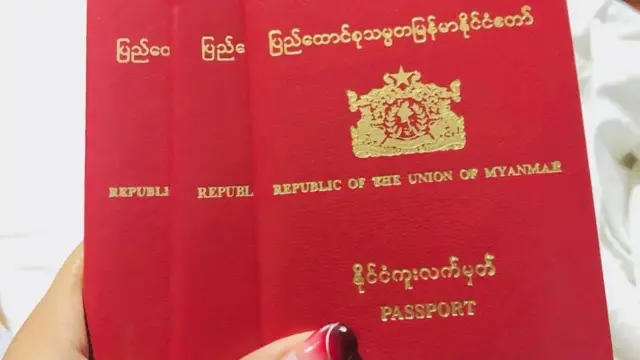 ပြည်ထောင်စုသမ္မတ မြန်မာနိုင်ငံတော် နိုင်ငံကူး လက်မှတ် အနီရောင်အဖုံးနဲ့ စာအုပ် ၃ အုပ်ကို ထပ်ပြီး အမျိုးသမီးတစ်ဦးက လက်ကကိုင်ထားတဲ့ပုံ