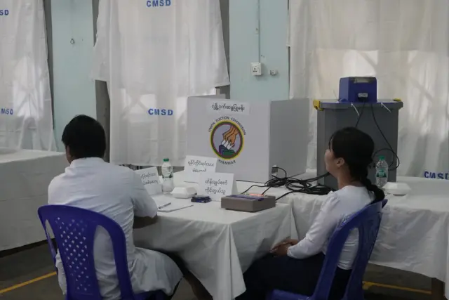 ရန်ကုန်မြို့ ပြည်သူ့ဆေးရုံကြီး ဝင်းထဲမှာ ဖွင့်ထားတဲ့ လသာမြို့နယ်အတွက် မဲရုံတစ်ရုံရဲ့ အတွင်းပိုင်း မြင်ကွင်းကို မြင်တွေ့ရတာဖြစ်ပါတယ်။ ရခိုင်တိုင်းရင်းသားကိုယ်စားလှယ်အတွက် မဲပေးစက် အရှေ့မှာ မဲကို စစ်ဆေးသူနဲ့ ထိန်းချုပ်စက်ကို ကိုင်တွယ်သူ မဲရုံဝန်ထမ်း ၂ ဦးကိုလည်း ပလက်စတစ်ထိုင်ခုံ အပြာပေါ်မှာ ထိုင်နေလျက်သားနဲ့မြင်တွေ့ရ