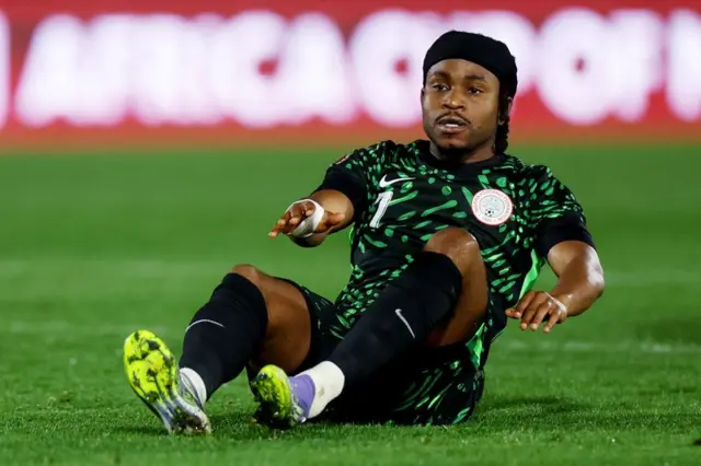 النيجيري أديمولا لوكمان مرتدياً لباس منتخبه الأسود والأخضر، ومستلقياً على أرض الملعب.