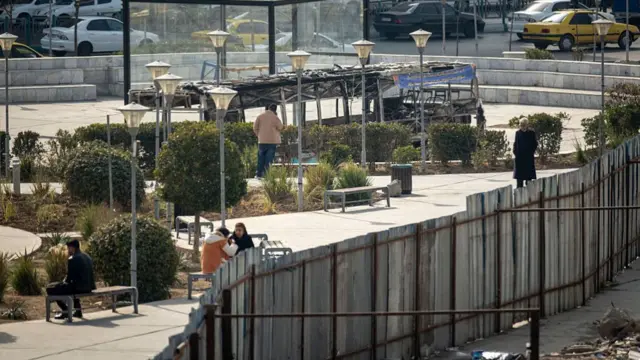 ورق‌های فلزی که اطراف پارک جوش داده شده و لاشه یک اتوبوس سوخته که برای نمایش گذاشته شده