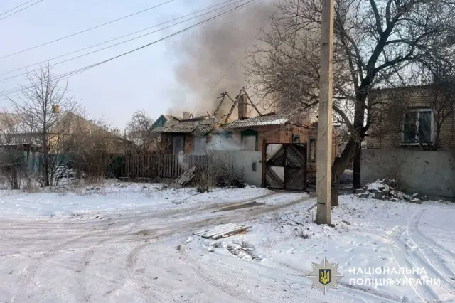 Одноэтажные дома в снегу, за ними виден дым.