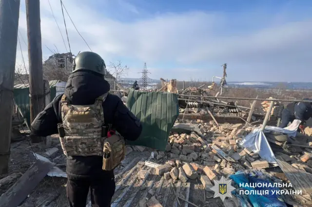 Человек в бронежилете смотрит на руины здания.