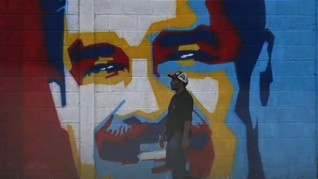 Homem passando em frente a um mural de Maduro