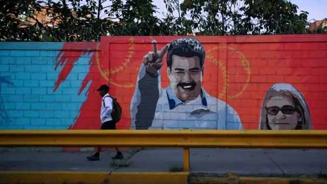 Una persona camina por delante de un mural de Nicolás Maduro y su esposa, la primera dama Cilia Flores.