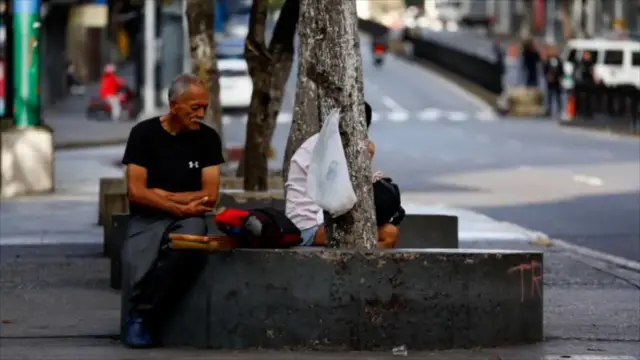 مردی در خیابان کاراکاس روی سکو کنار پیاده رو نشسته است