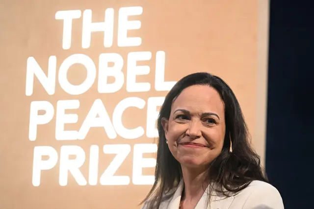 María Corina Machado sonríe, con el cartel del Premio Nobel de la Paz de fondo