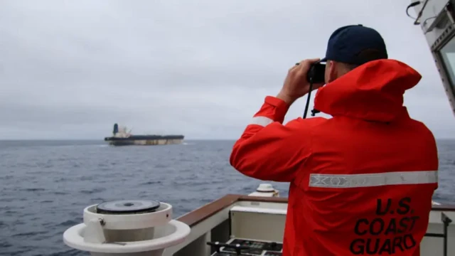 Представитель Береговой охраны США смотрит в бинокль на танкер Marinera