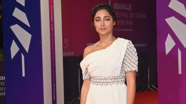 گلشیفته فراهانی با پیراهن سفید، ایستاده بر فرش قرمز مقابل بنرهای جشنواره فیلم کن