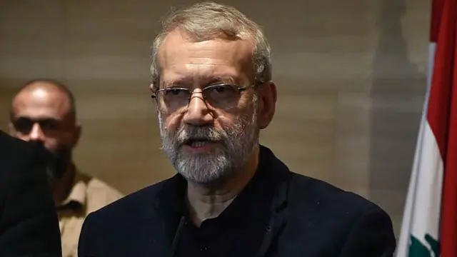 علی لاریجانی با کت و پیراهن سیاه جلوی پرچم لبنان
