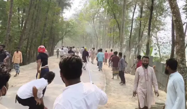 রাস্তায় দাঁড়িয়ে আছে অনেক মানুষ, দুই জনের হাতে লাঠি দেখা যাচ্ছে