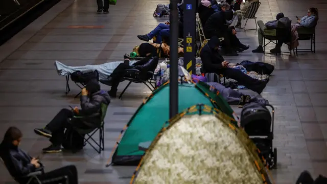 Палатки и люди, сидящие на складных стульях на платформе станции метро
