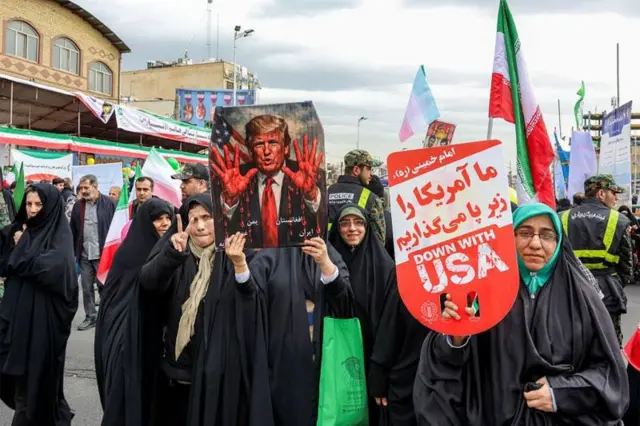 Mulheres marcham com um cartaz que retrata o presidente dos EUA, Donald Trump, com as mãos ensanguentadas em Teerã, em fevereiro de 2026
