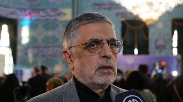 غلامحسین کرباسچی در محل اخذ رای با عینک و کت طوسی در حال مصاحبه