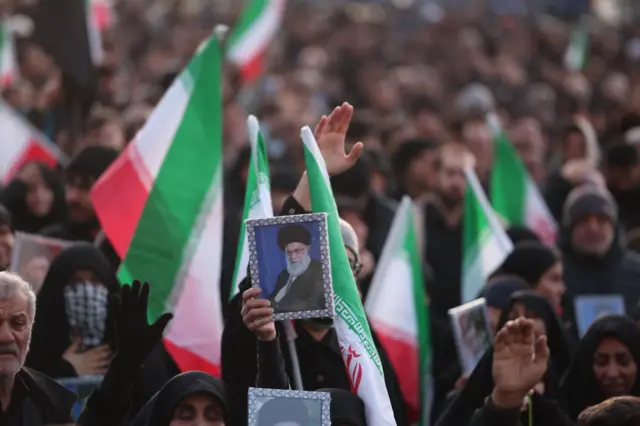 Dolientes en una plaza de Teherán con banderas de Irán y retratos de Alí Jamenei