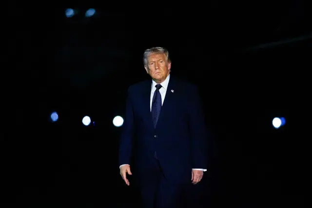 Trump Beyaz Saray'a dönüşü sırasında karanlıkta yürüyor.