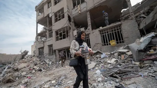 زنی در تهران در حال بیرون بردن وسایل خود از میان آوارهای ساختمان در تهران است