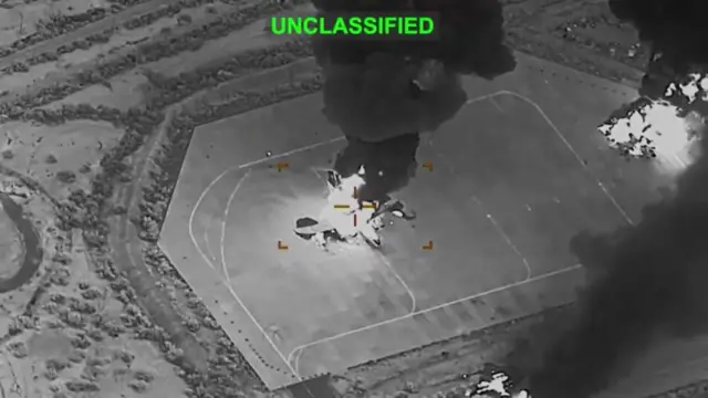 Hình ảnh đen trắng cho thấy mục tiêu là một chiếc máy bay đậu trên đường băng. Chiếc máy bay đang bốc cháy và khói bốc lên phía trên. Dòng chữ “unclassified” xuất hiện ở phía trên hình.