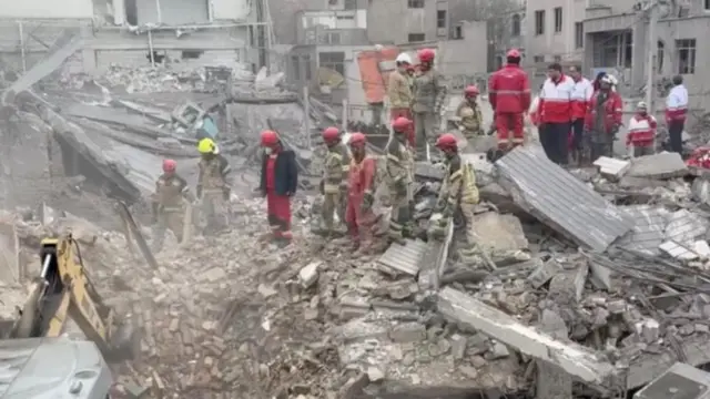 عمال إغاثة تابعون للهلال الأحمر الإيراني ومعهم جرافة يبحثون في أنقاض مبنى مدمر