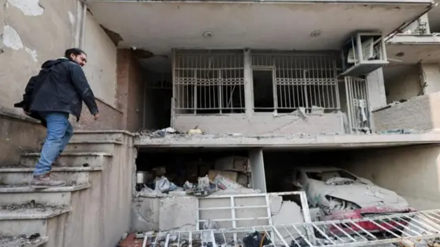 Tahran'da kısmen harabeye dönmüş apartmanının merdiveninden çıkan bir adam.