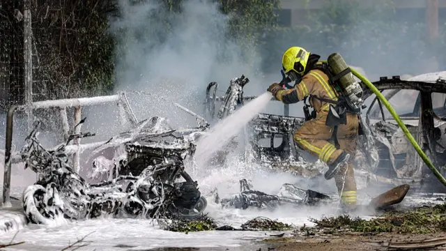 مامور آتش‌نشانی در حال خاموش کردن خودروهای سوخته در تل‌آویو