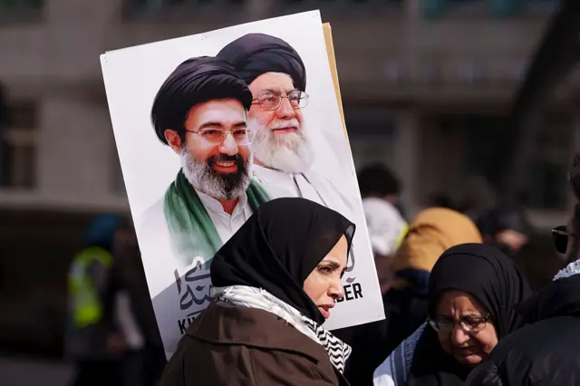 İranlı bir kadın, Hamaney ve oğlunun fotoğraflarını taşıyor.