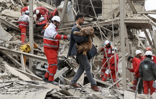 ABD-İsrail-İran çatışması sırasında, İran'ın başkenti Tahran'da, 16 Mart 2026 tarihinde, bir konut binasına düzenlenen saldırı yerinde acil durum ekipleri çalışırken bir adam köpeğini taşıyor.