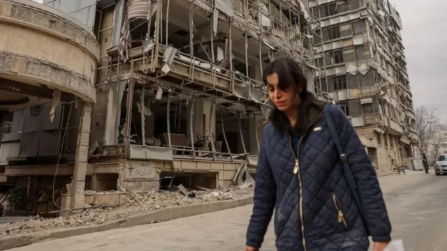 Yıkılmış binaların önünden yürüyen lacivert ceketli bir kadın
