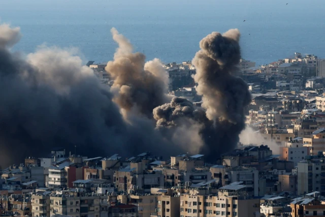 دخان يتصاعد بكثافة بين المباني المكتظة وفي المقابل يظهر البحر من بعيد. الصورة التقطت نهاراً.