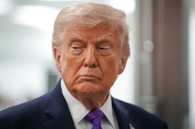 Perezida Trump areba muri 'camera' ahagana ku ruhande. Yambaye ikositimu.