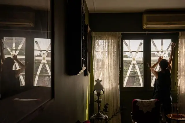 তেহরানের বাসিন্দারা ঘরের জানালায় টেপ লাগাচ্ছেন, যাতে বিস্ফোরণের ধাক্কায় কাঁচ ভেঙে ভেতরে ছিটকে না পড়ে।