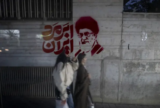 إيرانيتان تمران أمام صورة للمرشد الأعلى الراحل آية الله علي خامنئي مكتوب عليها بالفارسية "سوبرمان إيران" في طهران في 26 مارس/ آذار 2026