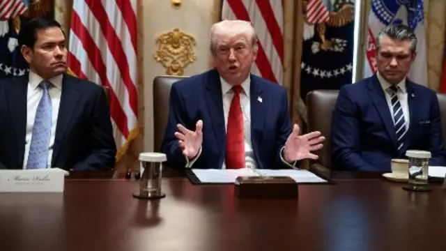 Marco Rubio, Donald Trump y Pete Hegseth sentados frente a una mesa de madera. Detrás, banderas de Estados Unidos.