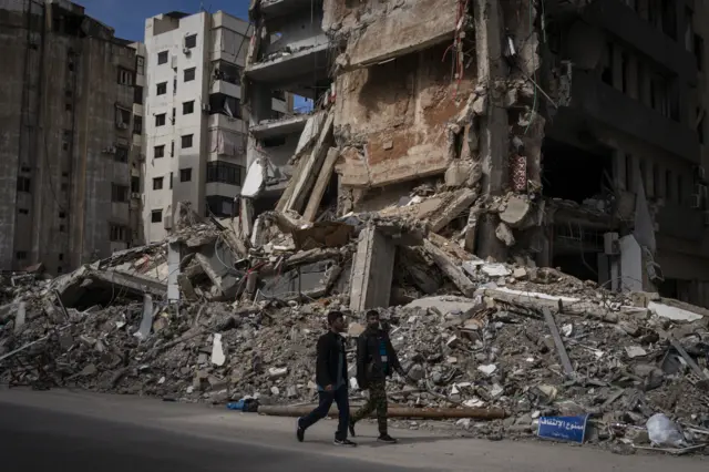 يسير رجلان أمام موقع استهداف نفّذه الجيش الإسرائيلي في منطقة الضاحية، بتاريخ 25 مارس/آذار 2026، في بيروت، لبنان.