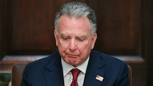 استیو ویتکاف با کت آبی و کراوات قرمز و پرچم آمریکا به یقه