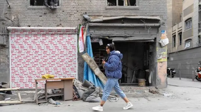 زن جوانی در حال راه رفتن مقابل ساختمانی تخریب شده