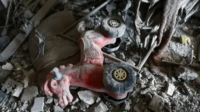 لعبة على شكل حصان بعجلات يمكن لطفل أن يركبها، لونها أحمر ومليئة بالغبار، ملقاة بين أنقاض مبنى سكني تضرر في طهران.