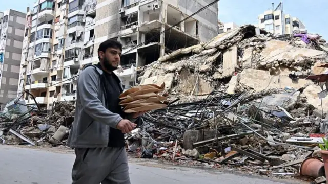 লেবাননের বৈরুতে হামলায় যুদ্ধে বিধ্বস্ত ভবনের সামনে দিয়ে হেঁটে যাচ্ছেন এক ব্যক্তি