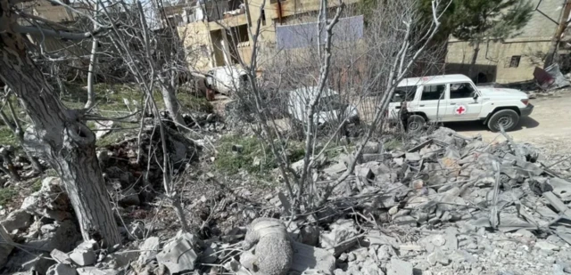 صورة تظهر أنقاضاً وركاماً وتظهر في الخلفية سيارة عليها شعار اللجنة الدولية للصليب الأحمر.