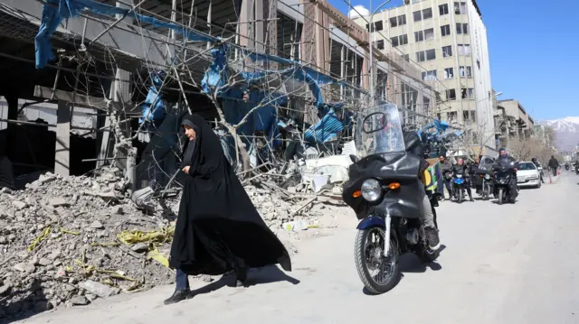 Женщина на фоне поврежденного здания в Тегеране
