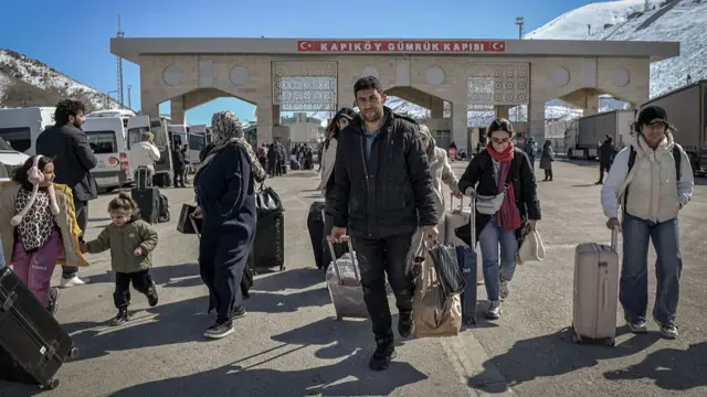 Personas con bolsos y maletas caminan en territorio turco tras pasar el cruzo fronterizo con Irán.