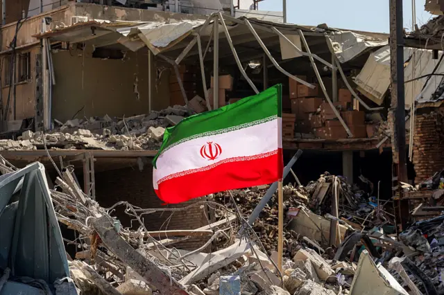 Una bandera de Irán izada en medio de los escombros de un edificio destruido.