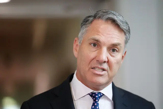 وزير الدفاع الأسترالي، ريتشارد مارلز يرتدي بدلة رسمية كحلية اللون وقميصاً أبيض وربطة عنق كحلية منقطة بلون وردي.